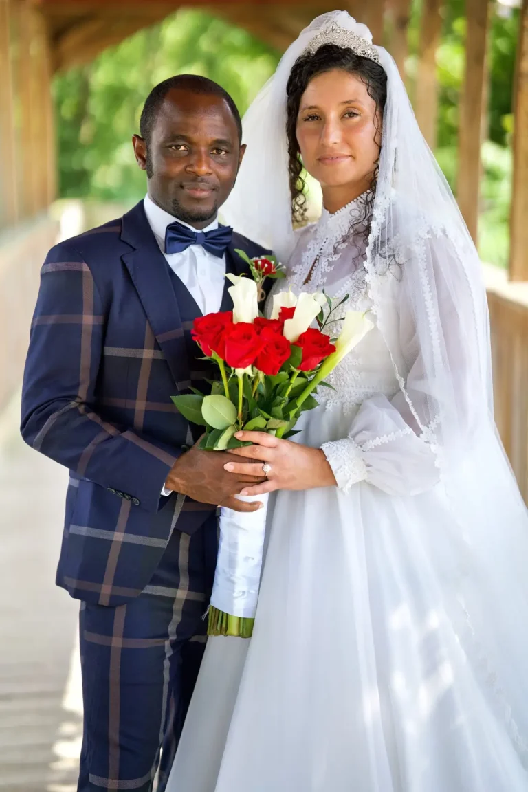 Bride and groom with red and white roses on a wooden bridge