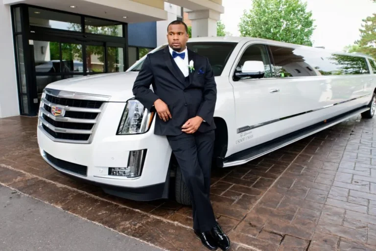 Groom in a tuxedo leaning on a white stretch limousine