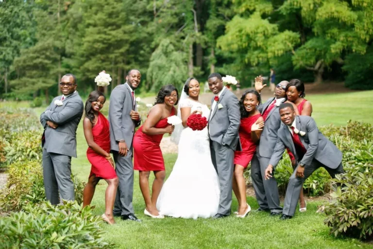 Wedding party in red and grey gathered around the couple on a garden lawn